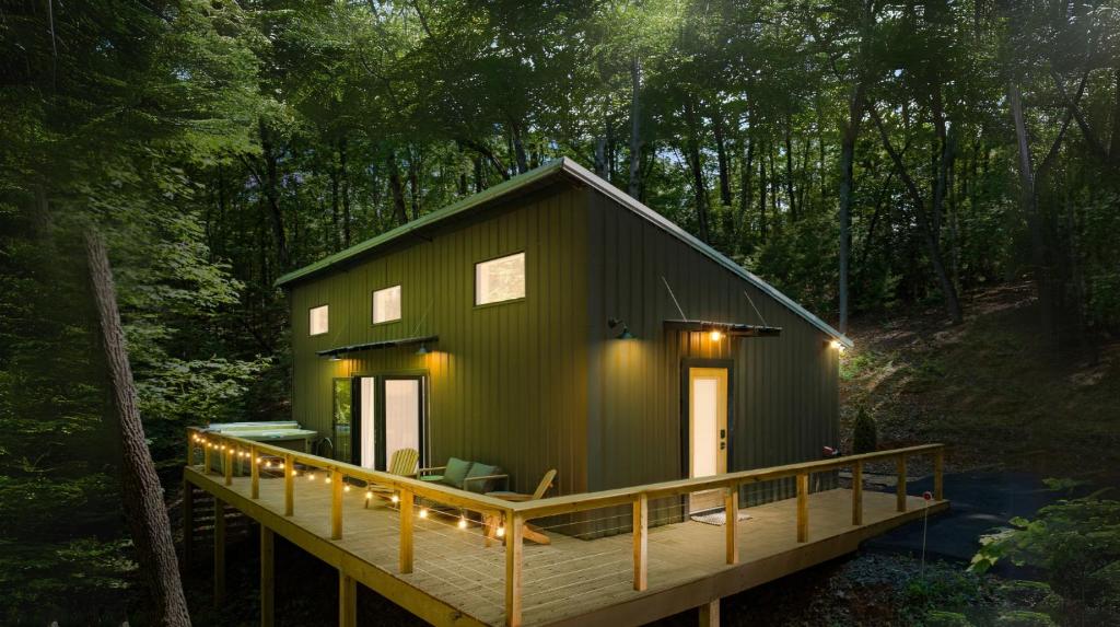 a green cabin with a deck in the woods at Couple's Cabin With Outdoor Movies, Firepit and Hot Tub - Rose Peak Loft in Blue Ridge