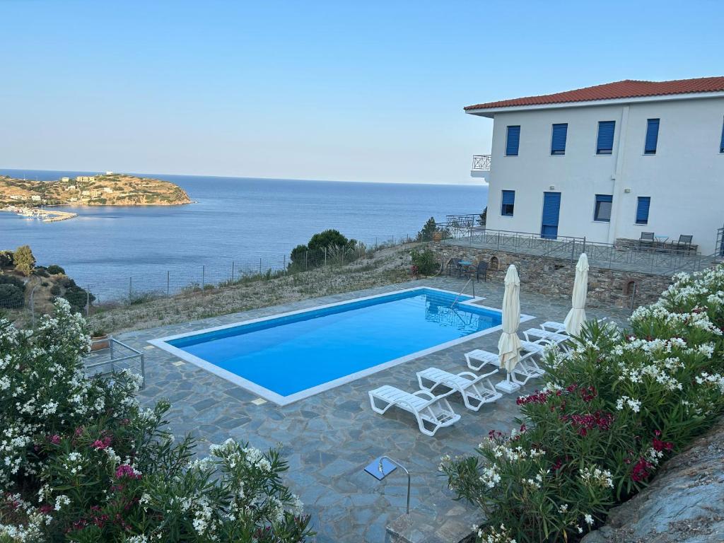 a swimming pool with chairs and a building and the ocean at Archontiko Dagmar in Áyioi Apóstoloi