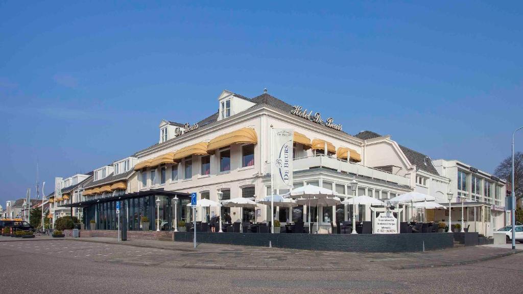 een groot wit gebouw met parasols op een straat bij Hotel De Beurs in Hoofddorp