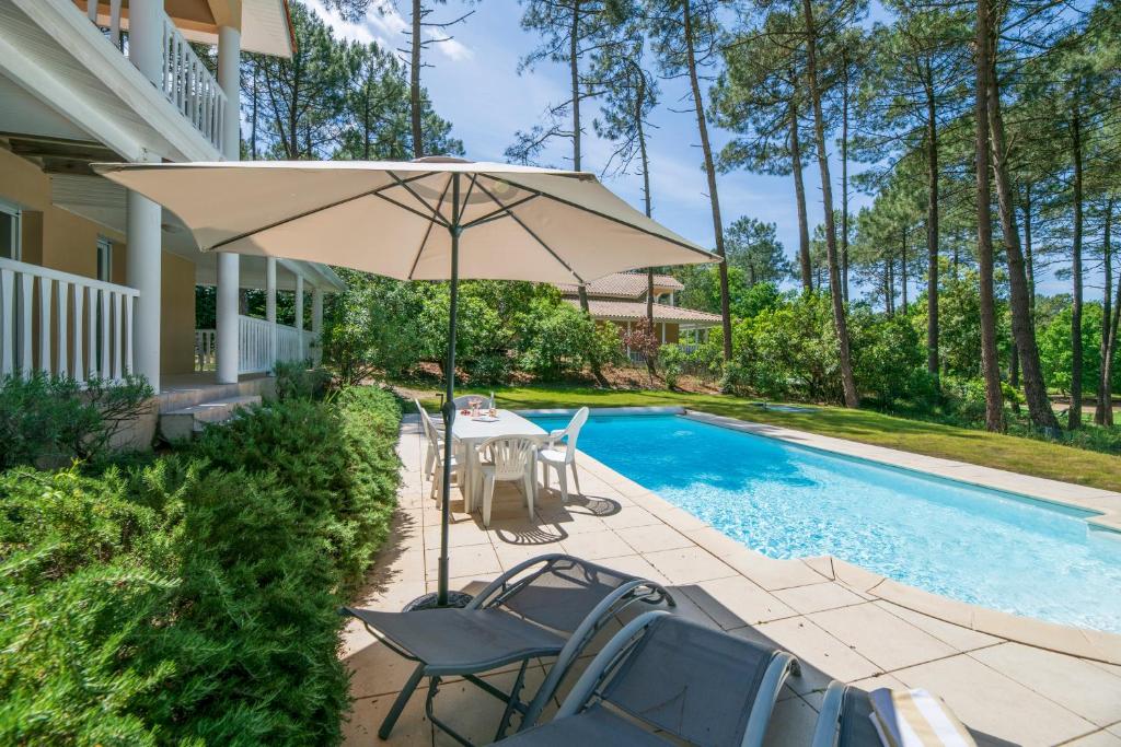 een terras met een tafel en een parasol naast een zwembad bij Lagrange Vacances - Eden Parc Golf in Lacanau-Océan