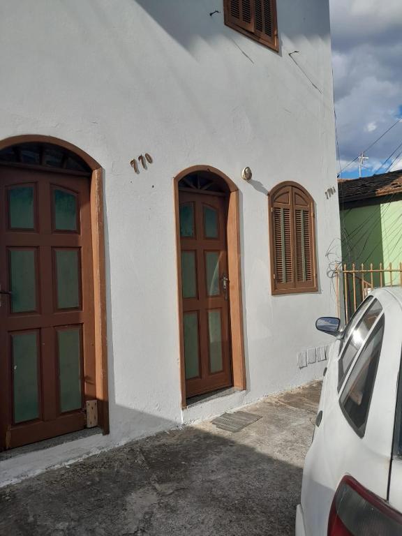 a white building with brown doors and a car parked outside at Apartamento a 300m do Centro e próximo a universidade federal in Diamantina