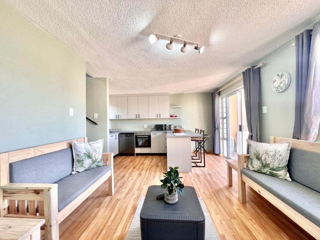 a living room with two blue couches and a kitchen at Fijnbosch Villa at Claptons in Jeffreys Bay