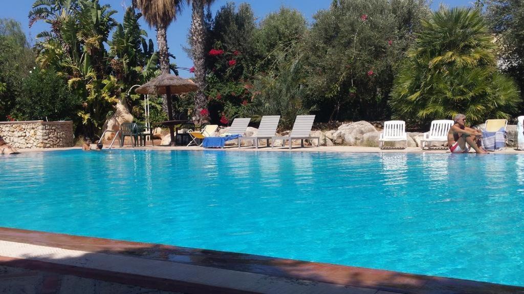 a large blue swimming pool with chairs and people in it at Le terrazze house with swimming pool in Terrasini in Terrasini