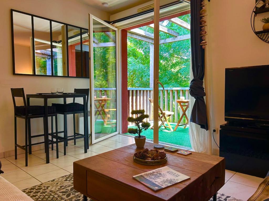 - un salon avec une table et une vue sur une terrasse couverte dans l'établissement Joli T2 niché dans les arbres au cœur du bassin, à Audenge