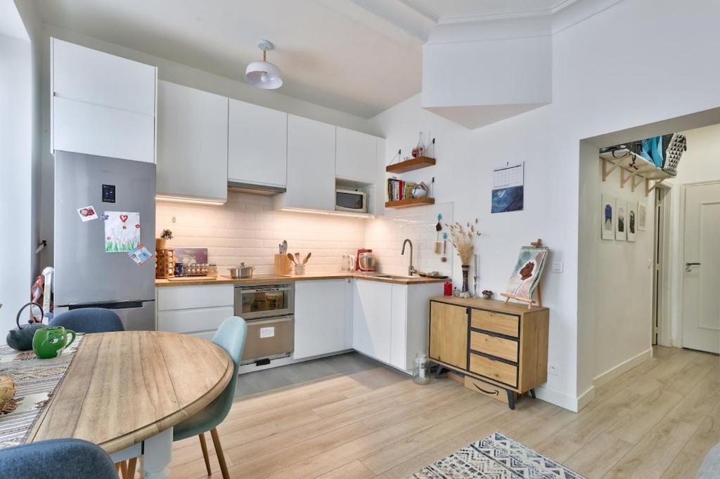 une cuisine avec des armoires blanches et une table en bois dans l'établissement Cosy et charmant appart 4 pers, à Paris