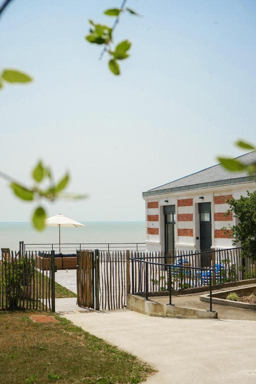 un bâtiment sur la plage avec une clôture et un parasol dans l'établissement Loft vue mer - Angoulins - Villa Oasis, à Angoulins-sur-Mer
