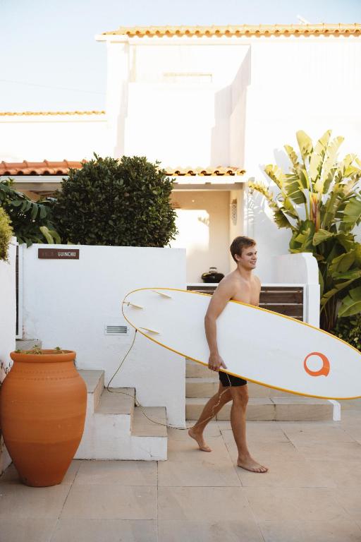 a man walking with a surfboard in front of a house at Sea'Ya Thoughtful Stays - Villas in Cascais