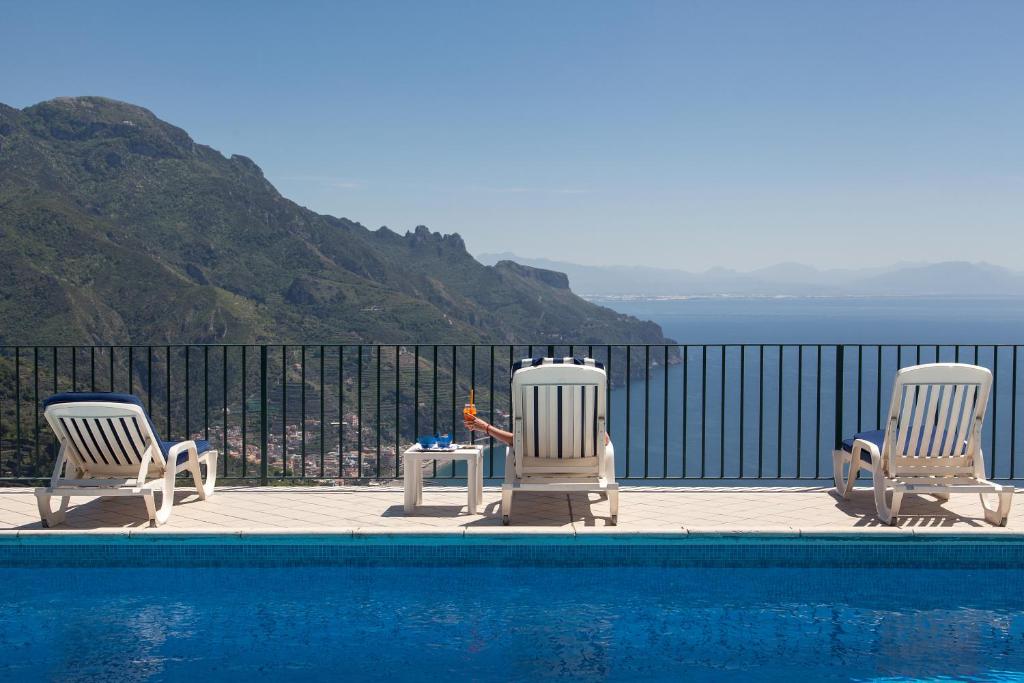 drie stoelen en een tafel naast een zwembad bij Hotel Graal in Ravello