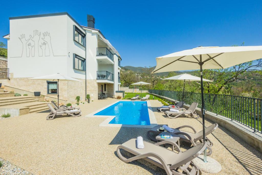 a villa with a swimming pool with chairs and an umbrella at Villa Manus - Boutique Apartments in Lovran
