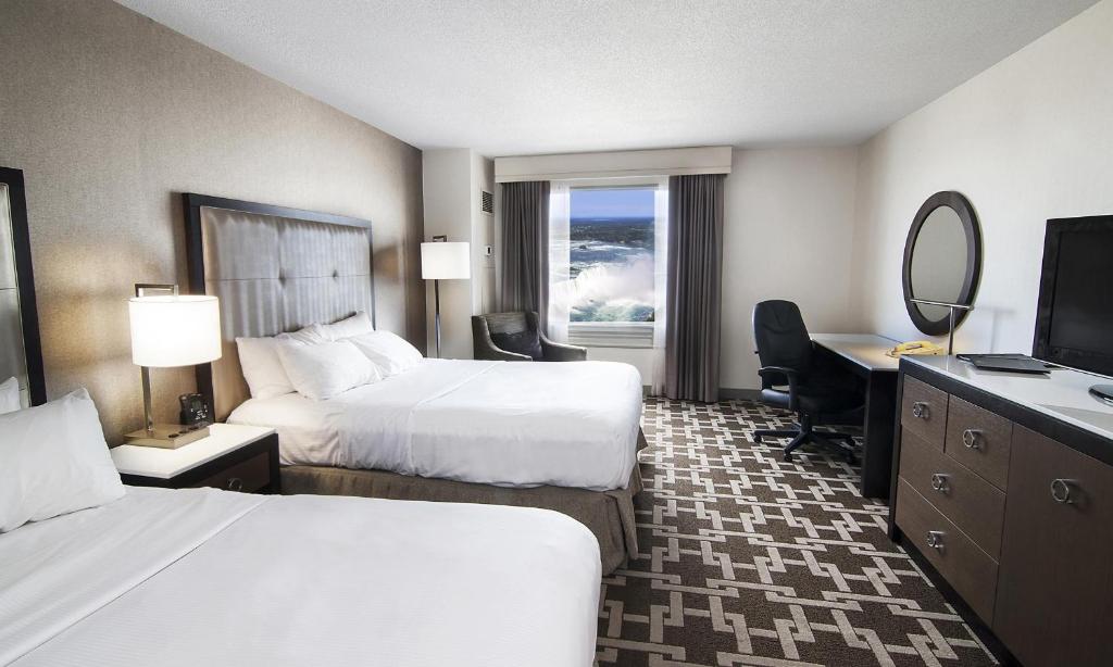 a hotel room with two beds and a desk and a television at Hilton Niagara Falls/ Fallsview Hotel and Suites in Niagara Falls
