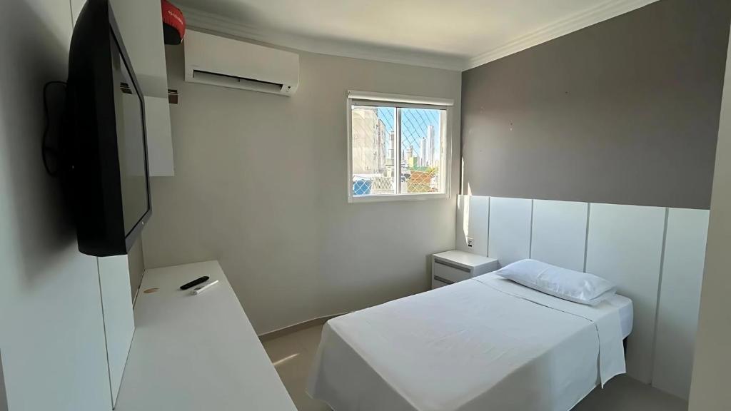 um pequeno quarto branco com uma cama e uma televisão em Apto Almeida e Moraes Aconchegante em BC no Balneário Camboriú