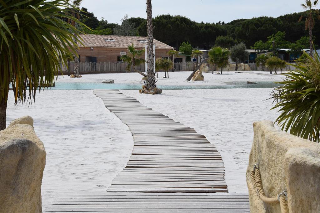 a wooden walkway on a sandy beach with palm trees at Mobil-Home Premium Camping 5 étoiles Valras-Plage Domaine La Yole in Vendres