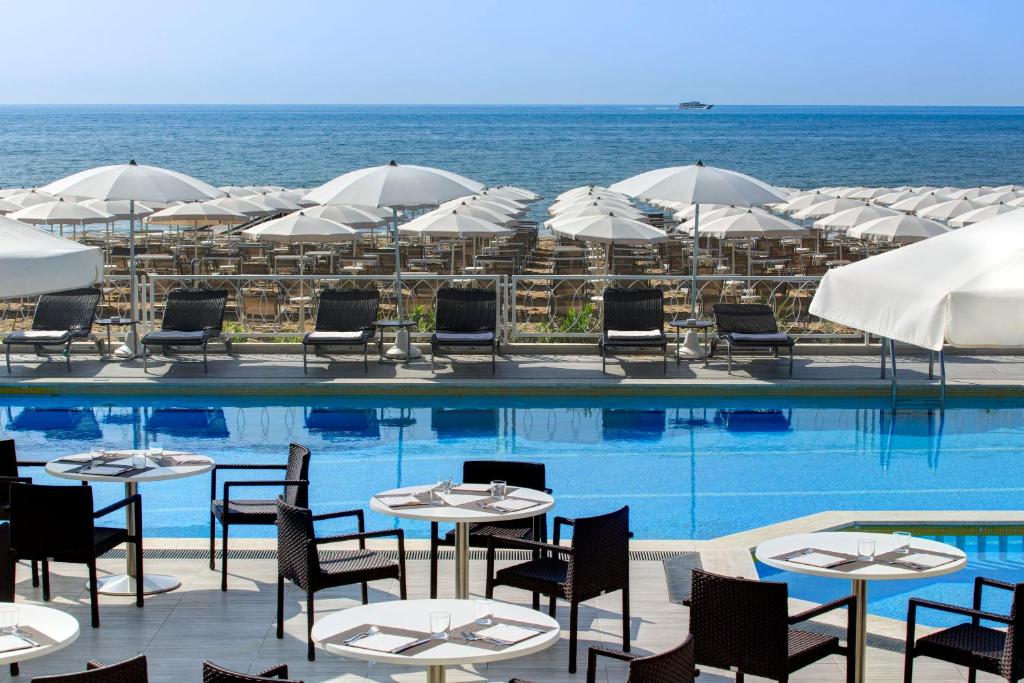 una piscina con tavoli, sedie e ombrelloni di Hotel Byron Bellavista a Lido di Jesolo