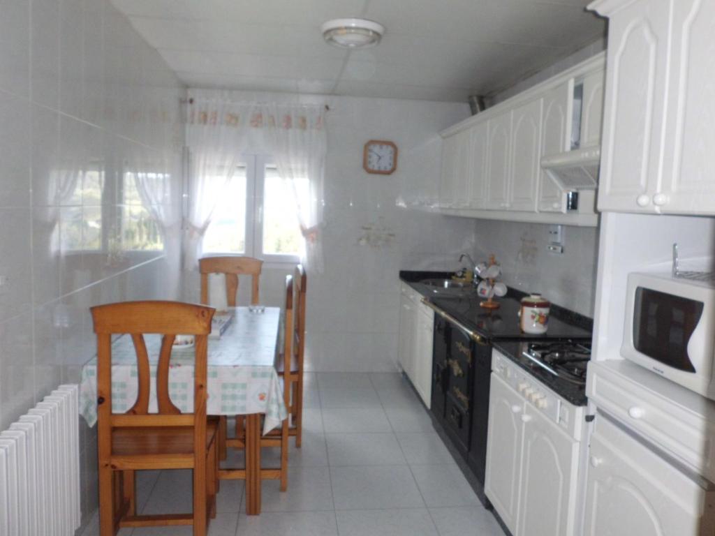 cocina con armarios blancos, mesa y sillas en Apartamento Casa Jeronimo, en Taramundi