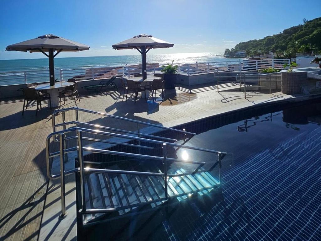 a swimming pool with tables and umbrellas next to the ocean at Apartamento Praia do Centro Pipa in Pipa