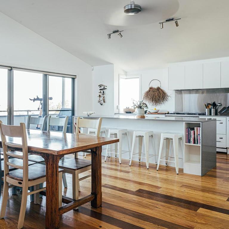 a white kitchen with a wooden table and chairs at Anglesea by Bangalay in Shoalhaven Heads