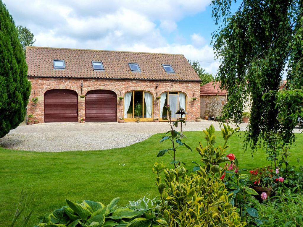 a brick house with two garage doors in a yard at Wold View Cottage in Rillington