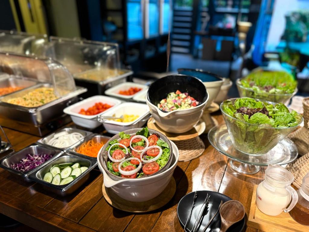 A close-up of a self-serve breakfast spread with salad, vegetables, toppings and dairy drinks.