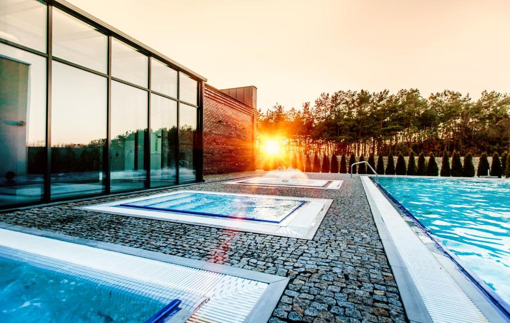 a swimming pool in front of a building with the sun setting at Lawendowe Termy in Uniejow