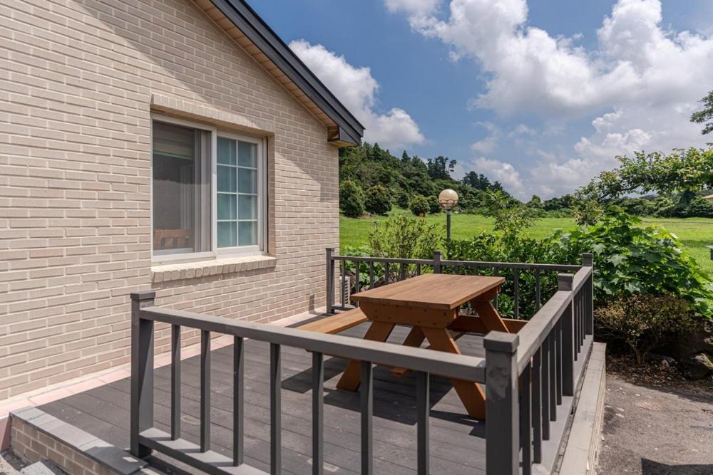 una mesa de picnic de madera en una terraza junto a un edificio en Jeju Albam Oreum House Pension, en Jeju