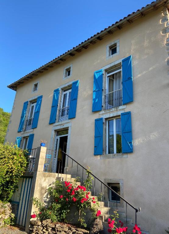 un bâtiment avec des fenêtres à volets bleus et des fleurs dans l'établissement La Commingeoise aux portes du bois, 