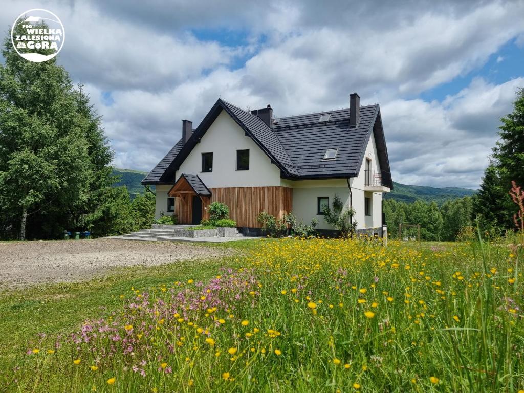 a white house with a black roof and a field of flowers at Pod Wielką Zalesioną Górą in Wetlina