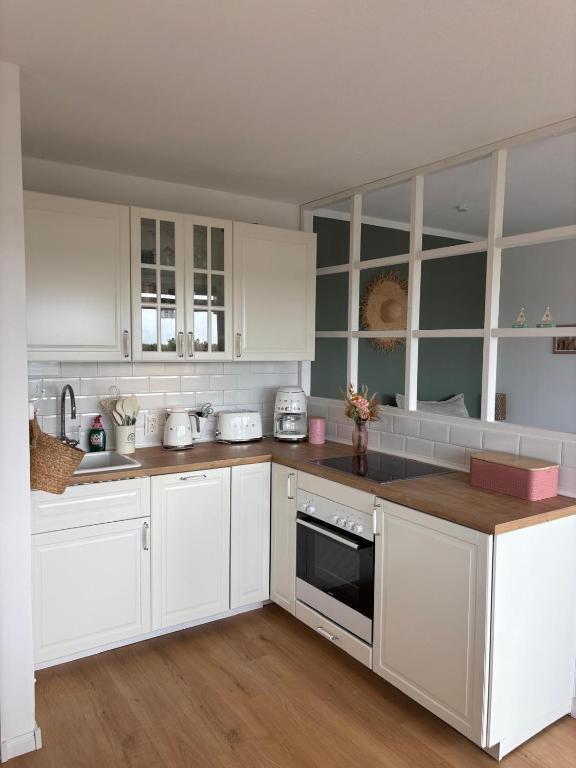 a white kitchen with white cabinets and wooden floors at Ferienwohnung kleiner Sonnenschein Großenbrode Ostsee in Grossenbrode