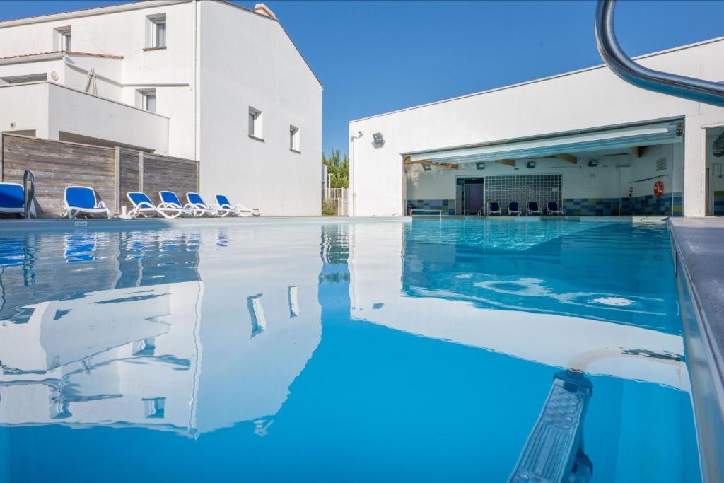 a swimming pool with chairs and a building at Résidence Prestige Odalys Le Domaine des Pins in Noirmoutier-en-l'lle
