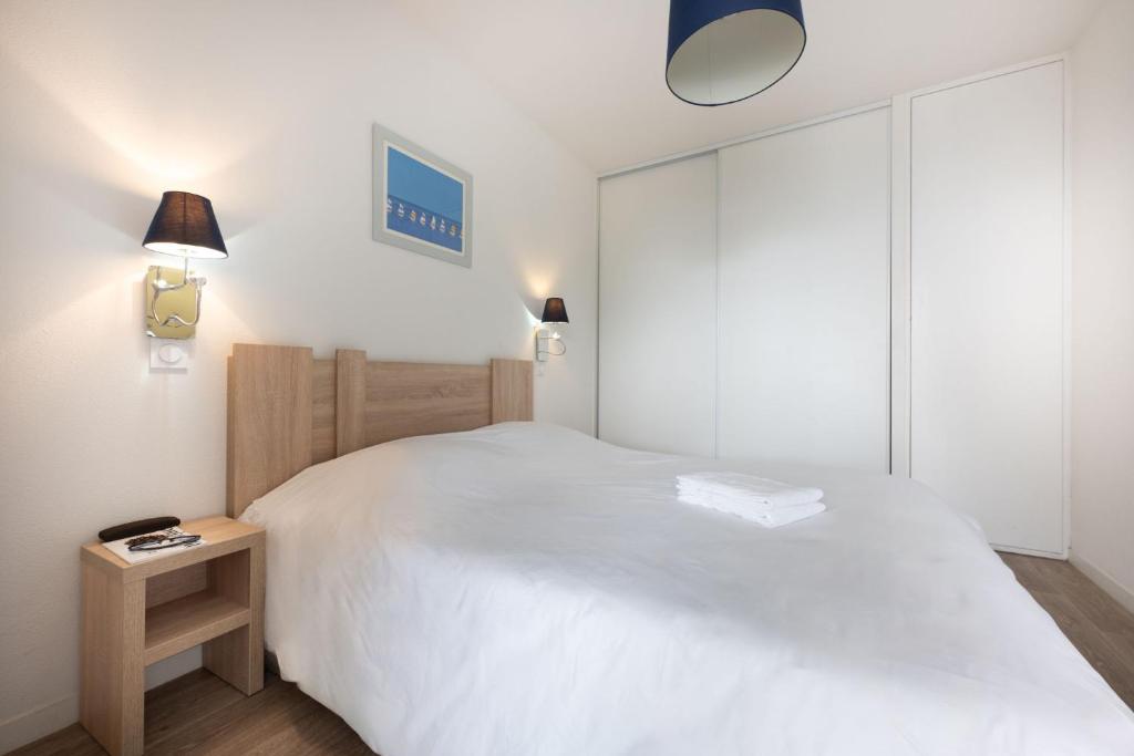 a bedroom with a large white bed and a lamp at Résidence Prestige Odalys Le Domaine des Pins in Noirmoutier-en-l'lle