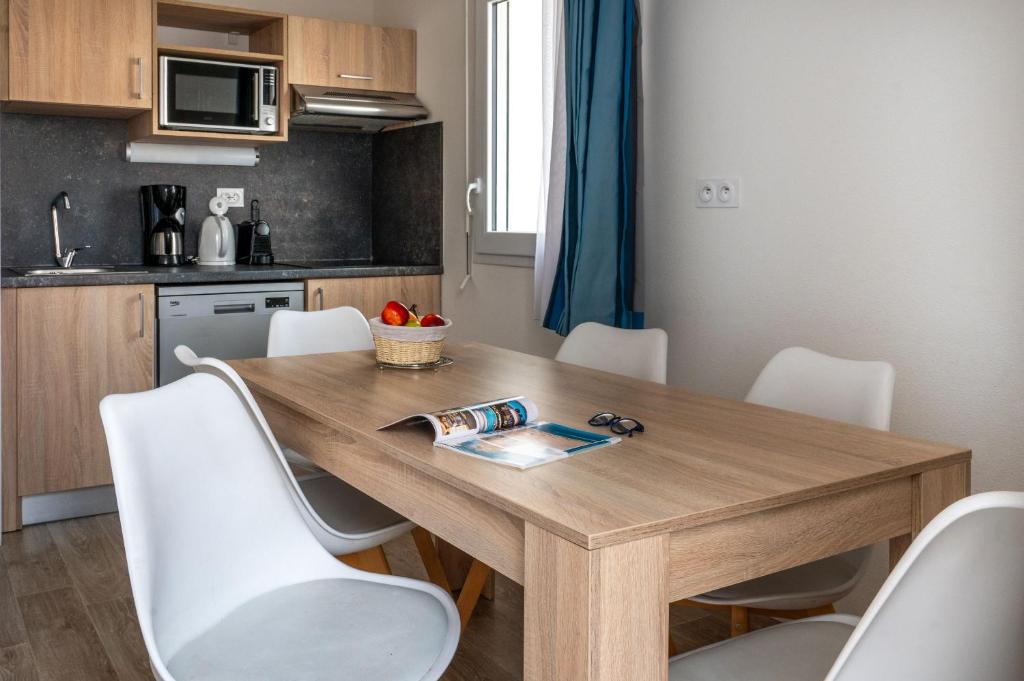 a kitchen with a wooden table and white chairs at Résidence Prestige Odalys Le Domaine des Pins in Noirmoutier-en-l'lle