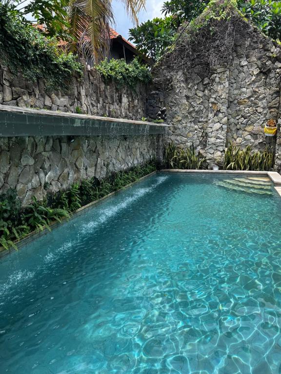 a swimming pool with blue water next to a stone wall at Remedy in Lagas in Ubud