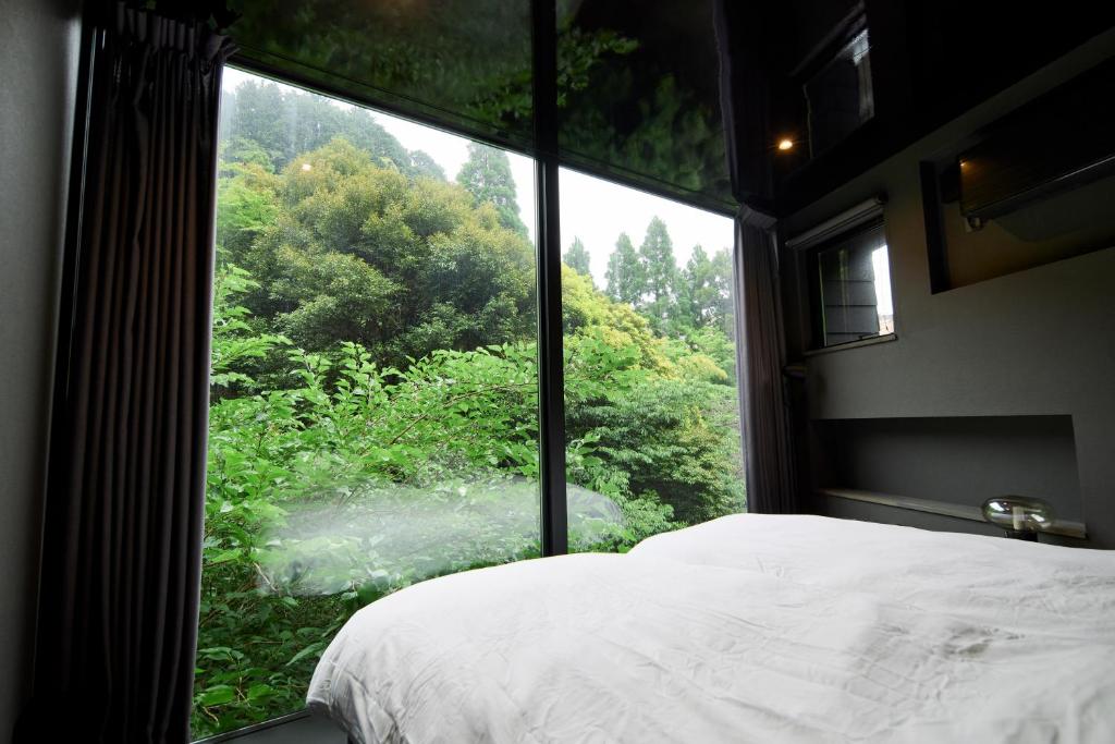 a bedroom with a large window looking out at a forest at COCO VILLA 奥湯河原-Sauna- in Yugawara