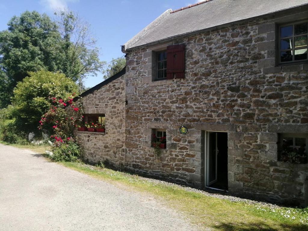 un vieux bâtiment en pierre avec des fleurs aux fenêtres dans l'établissement Gîte du Moulin de Brendouez, à Guissény
