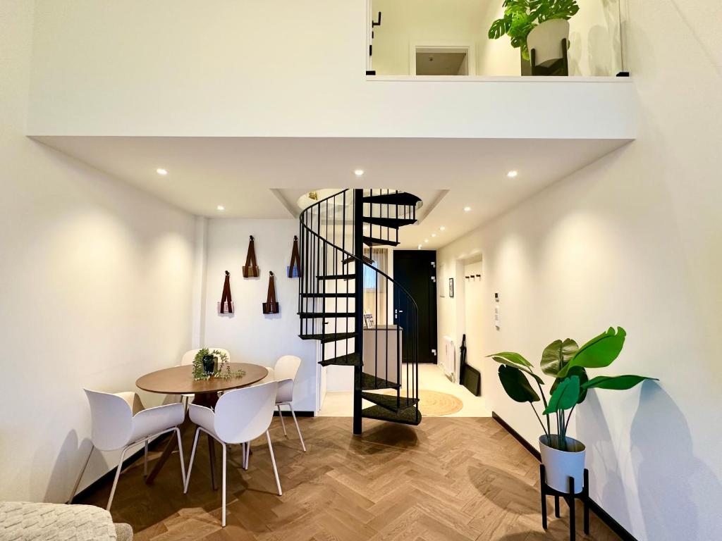 a room with a table and chairs and a spiral staircase at Das Alpenzeit Loft mit Balkon und Grimmingblick in Bad Mitterndorf