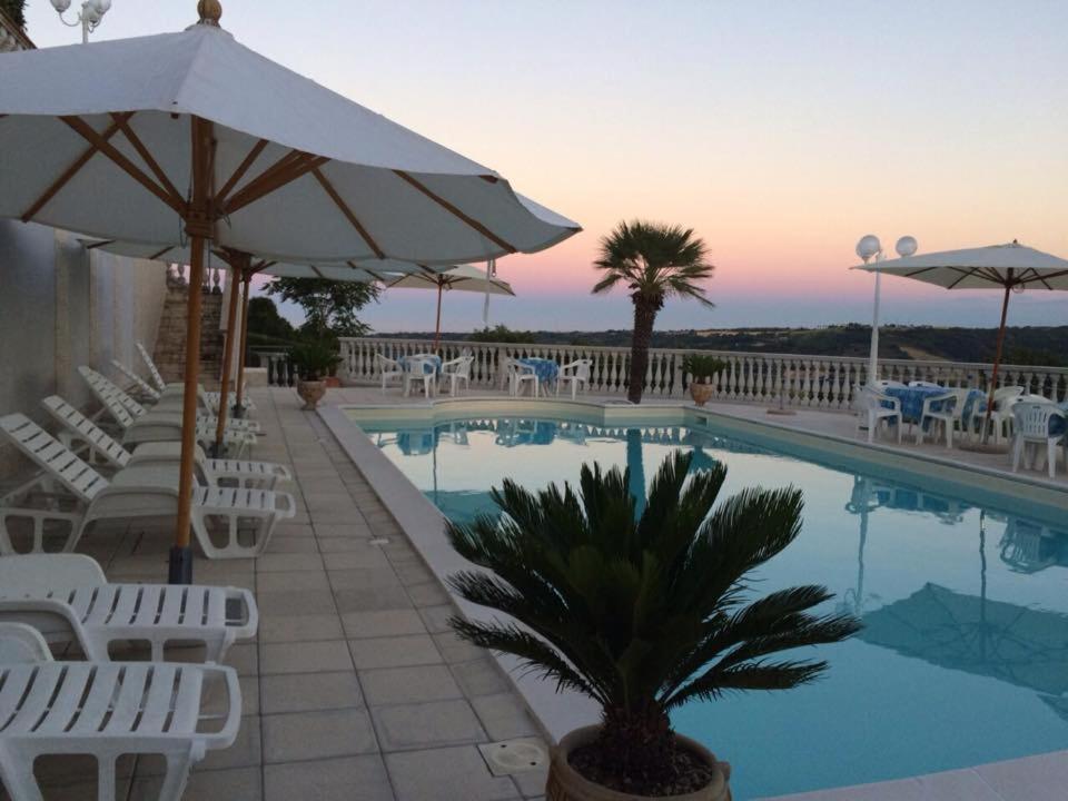 een zwembad met witte stoelen en een parasol bij Hotel Villa Aniana in Massignano