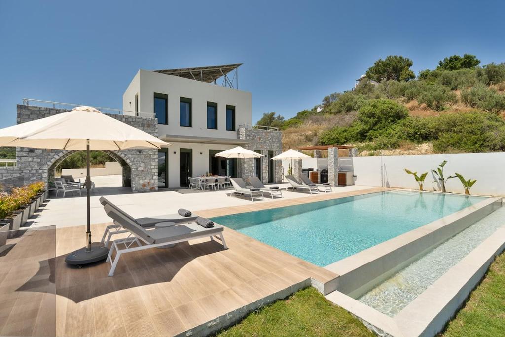 a pool with chairs and an umbrella and a building at Villa Meraki in Stalos