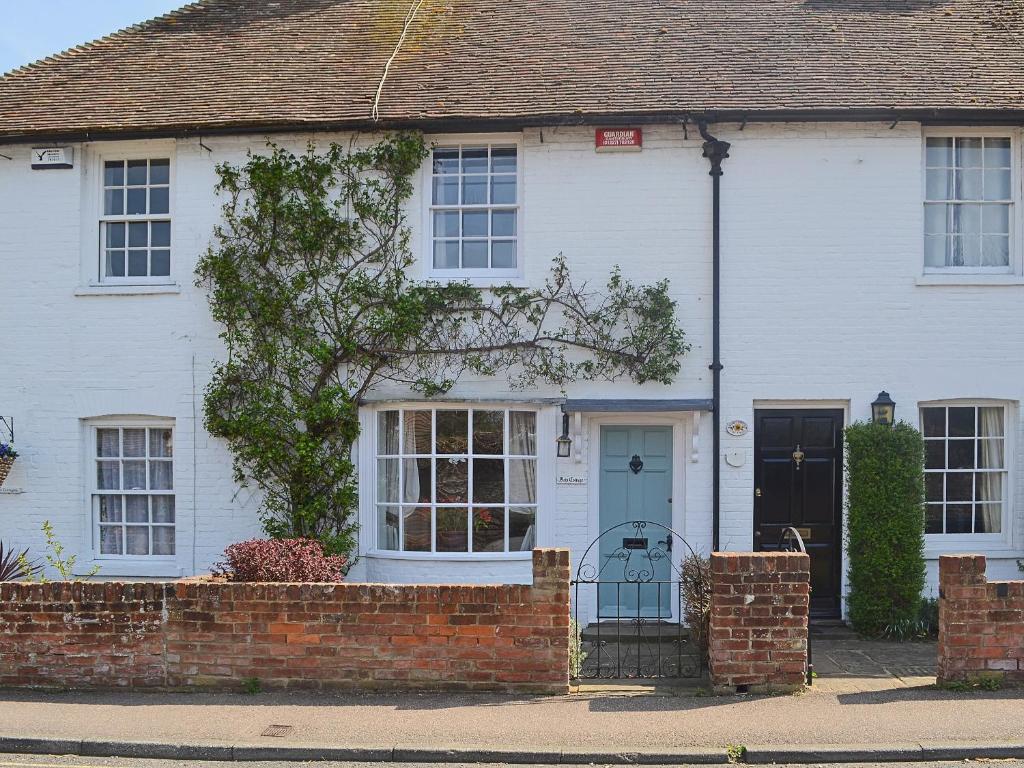 une maison blanche avec une porte bleue et une clôture en briques dans l'établissement Bow Cottage, à Fordwich