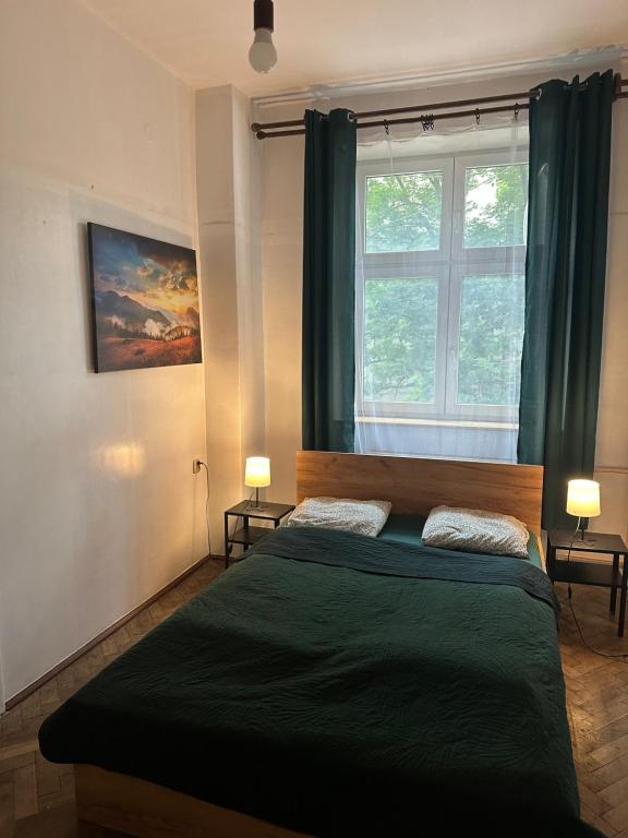 a bedroom with a bed with green sheets and a window at City Center Rooms in Kraków