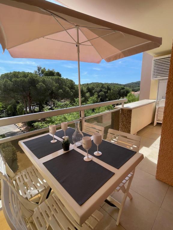 - une table avec des verres et un parasol sur le balcon dans l'établissement bel appartement climatisé près de la plage, à Bormes-les-Mimosas