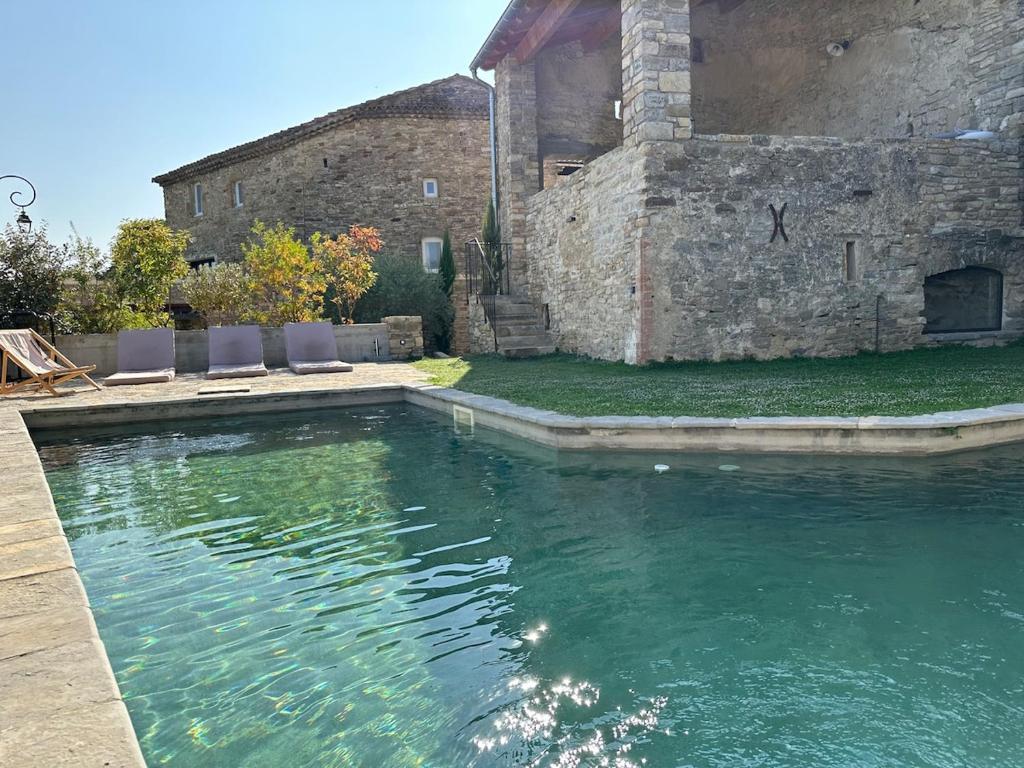 - une piscine avec des chaises en face d'un bâtiment dans l'établissement Maison de village avec piscine, à Saint-Étienne-de-Lolm