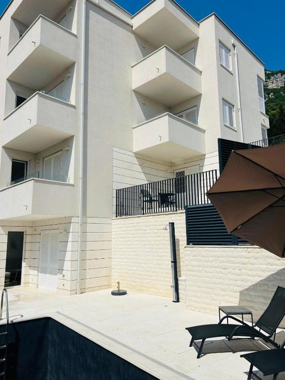 a large white building with two chairs and an umbrella at Apartmani Villa Antea in Klek