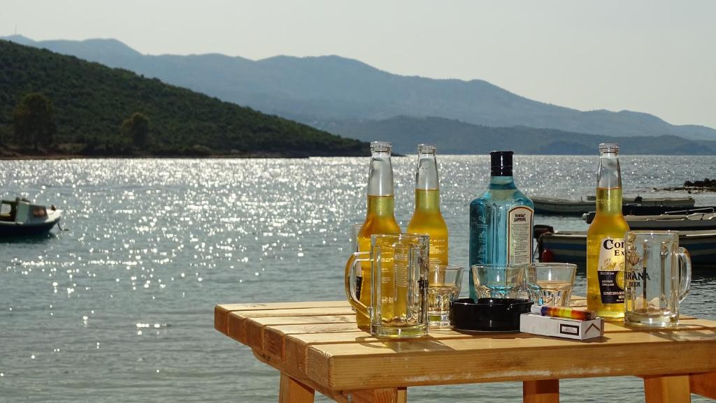 - une table en bois avec des bouteilles et des verres sur l'eau dans l'établissement Vila Reni & Risi, à Ksamil