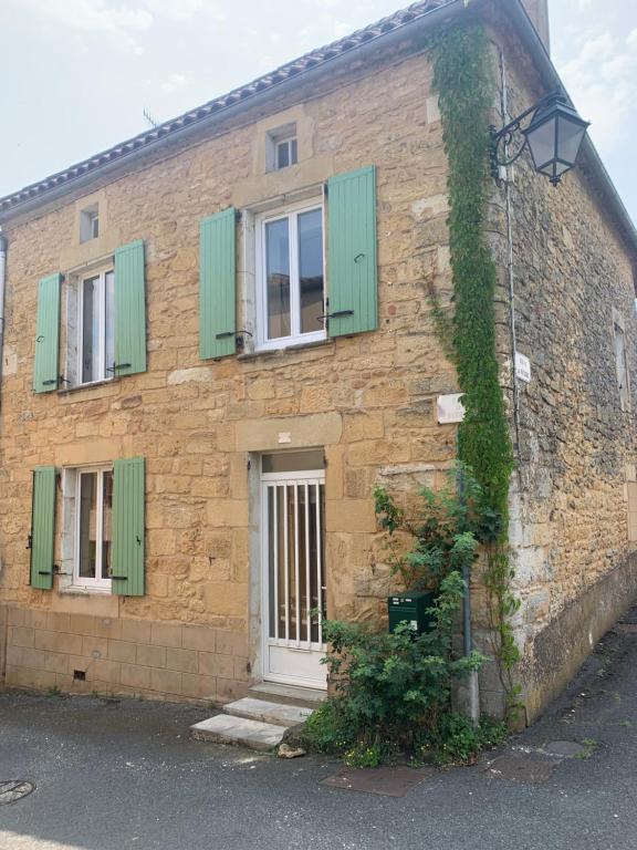 un bâtiment en briques avec des volets verts et une porte blanche dans l'établissement Maison de village, à Belvès