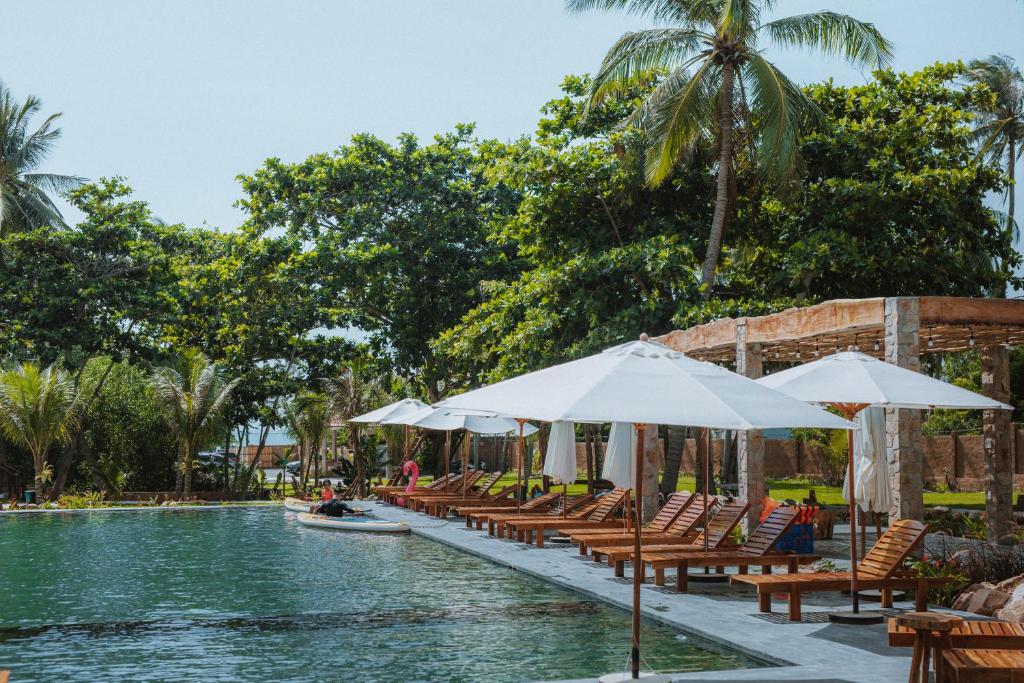 a pool with chairs and umbrellas next to a resort at Charm Hon Rom Villas Resort in Ấp Long Sơn