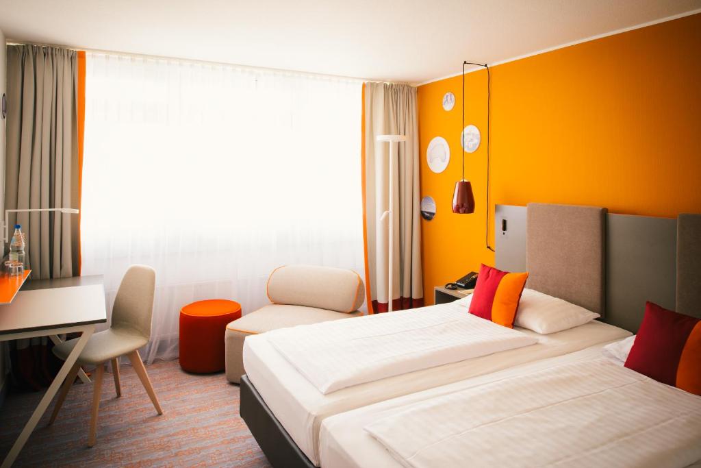 a hotel room with two beds and a desk at Vienna House Easy by Wyndham Günzburg in Günzburg