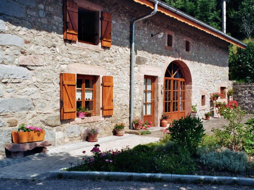 a stone house with wooden doors and flowers in front of it at Gîte du Champ du Bois : Confort au cœur des Vosges - FR-1-589-820 in Le Tholy
