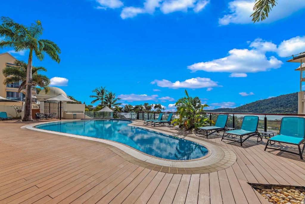 a swimming pool with blue chairs and a deck at The Drift - Airlie Two in Airlie Beach