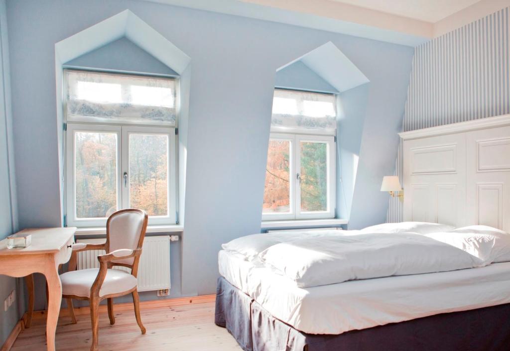 a bedroom with a bed and a desk and two windows at Gut Sarnow - Hotel, Restaurant und Reitanlage in Schorfheide