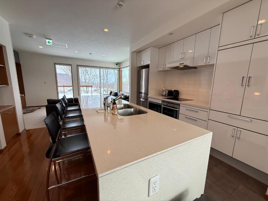 a kitchen with white cabinets and a large island with chairs at Yutaka 2 in Kutchan