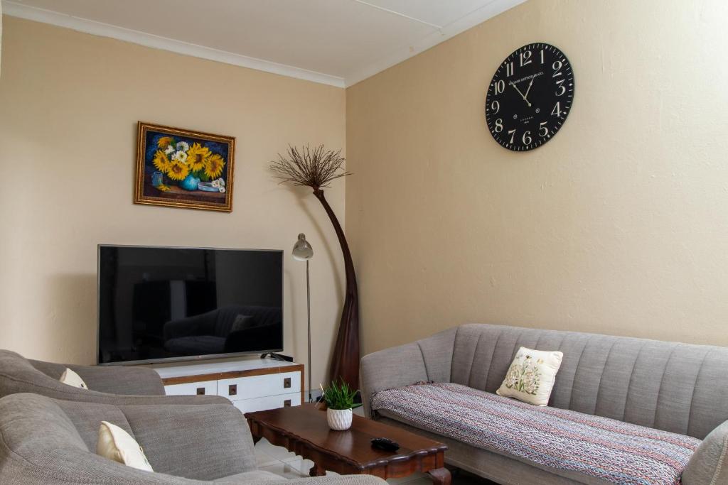 een woonkamer met een bank en een klok aan de muur bij Roots Self Catering Unit 1 in Port Elizabeth